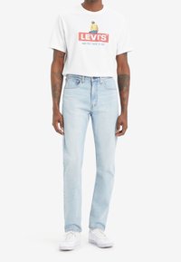 Vit bomullströja med en röd Levi's-logga och grafik, tillsammans med ljusblå denimjeans och vita sneakers. Avslappnad passform, korta ärmar.