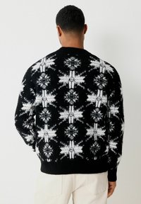Pull en tricot noir avec un motif de flocon de neige blanc, col rond, ourlet côtelé et tissu texturé. Vue arrière montrant des détails complexes.