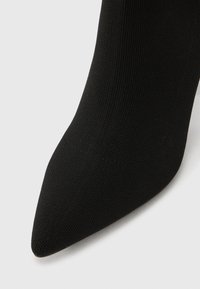 Melns adīts puszābaks ar smailu purngalu un gludu tekstūru uz balta fona.