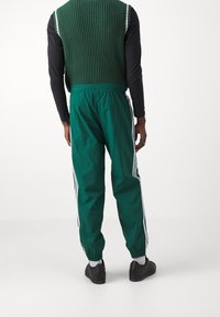 Gröna, lätta träningsbyxor med elastisk midja och muddar, med tre vita ränder längs sidorna, tillsammans med en ribbad grön väst.