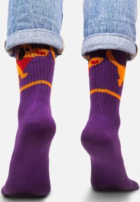 Fioletowe skarpety z pomarańczowym wzorem psa i czerwonymi akcentami. Żebrowana tekstura i bezszwowa konstrukcja palców. Styl z mankietem w połączeniu z dżinsami.