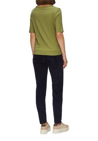 Oliwkowa, prążkowana bluzka z krótkim rękawem, w połączeniu z ciemnogranatowymi spodniami i beżowymi trampkami na platformie, widok z tyłu.