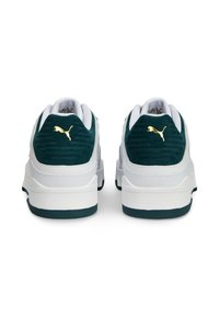 Hvide sneakers med grønne ruskindsdetaljer, teksturerede bagpaneler og guld logo. Tykk hvid sål med grøn bund, der har lagdelte designelementer.