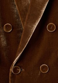 Bruine fluwelen blazer met een dubbelzijdig ontwerp, met afgeknipte revers en ronde, met stof beklede knopen. Soepele textuur met een glanzende afwerking.