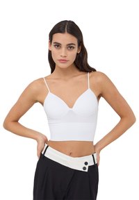 Top corto bianco a costine con spalline sottili e scollatura profonda, abbinato a pantaloni neri a vita alta con una vita a contrasto.
