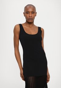 Musta hihaton mekko, jossa on istuva yläosa ja fringed-helma. Valmistettu ribbikankaasta, jossa on pyöreä pääntie ja sileä pinta.