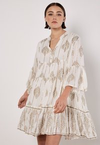 Weißes Kleid mit goldenen detaillierten Mustern, plissierter Textur, Knopfleiste vorne und Glockenärmeln. Der ausgestellte Saum trägt zur Gestaltung bei.