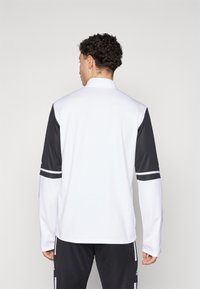 Hvid quarter-zip pullover med sorte ærmer, der har to horisontale hvide striber på ærmerne og et glat, tekstureret stof.