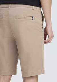 Pantalones cortos beige de mezcla de algodón, con una textura suave, corte recto y dos bolsillos traseros con una pequeña etiqueta de logo.