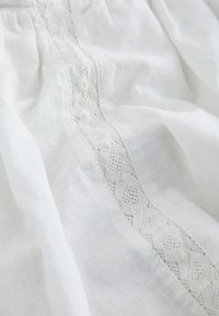 Witte stof met een delicate kanten strook met een diamantpatroon, zacht gevouwen en gedrapeerd.