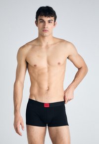 Schwarze Boxershorts aus einem glatten Stoff, mit einem roten Logo-Bund. Das Design ist körperbetont mit einem mittelhohen Schnitt.