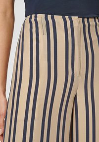Beige broek met marineblauwe verticale strepen, met een strakke taille, zijzakken en een soepele stoftextuur.
