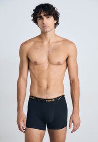 Schwarze Herren-Boxershorts mit einem elastischen Bund, der ein orangefarbenes Nike-Logo zeigt. Der Stoff wirkt glatt und dehnbar, konzipiert für Komfort.