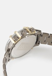 Orologio cronografo argento e oro con cassa in acciaio inossidabile, più tasti di pressione e bracciale a maglie, con un fondo liscio e inciso.