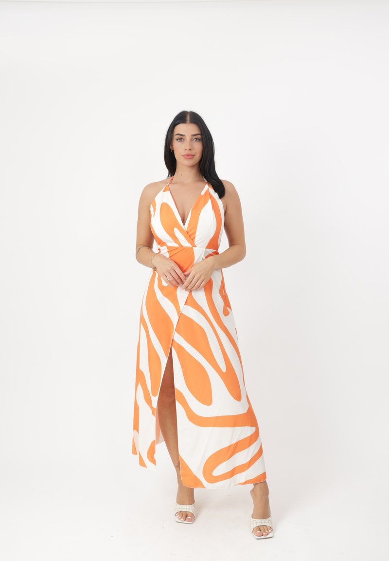 Kleid mit orange-weißer abstrakter Musterung, Halterneck-Design, mit einem Schlitz vorne und fließendem Stoff. Ergänzt mit hellfarbener Fußbekleidung.