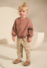 Brązowy sweter, spodnie w panterkę i brązowe buty. Miękka tekstura i luźny krój. Spodnie mają elastyczny pasek w talii i boczne kieszenie.