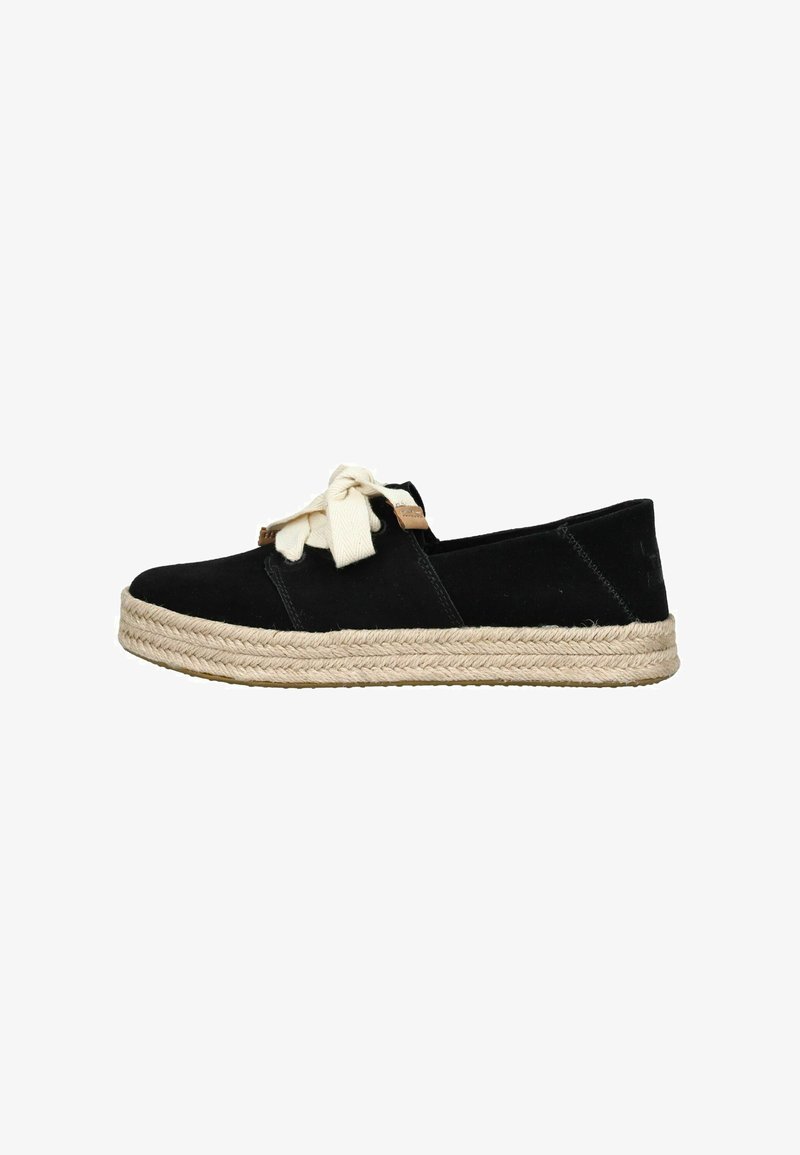 Zwarte espadrille met dikke gevlochten juten zool en grote strik van crèmekleurige stof als veters, zijaanzicht op witte achtergrond.