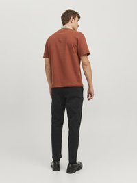 Rostfarbene Kurzarm-T-Shirt mit Rundhalsausschnitt, kombiniert mit schwarzen Slim-Fit-Hosen und schwarzen Schuhen, von hinten betrachtet.