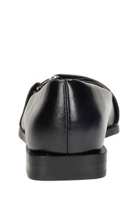 Mocassini in pelle nera con punta arrotondata, suola piatta e cuciture minime. Presentano una texture liscia e un design sobrio.