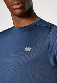 Marineblaue Sportshirt aus strukturiertem, leichtem Material, mit einem silbernen New Balance-Logo auf der linken Brust und Rundhalsausschnitt.
