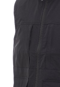 Černá vesta s texturovanou tkaninou, která má přední zip, dvě velké našité kapsy a minimalistický design. Povrch je hladký.