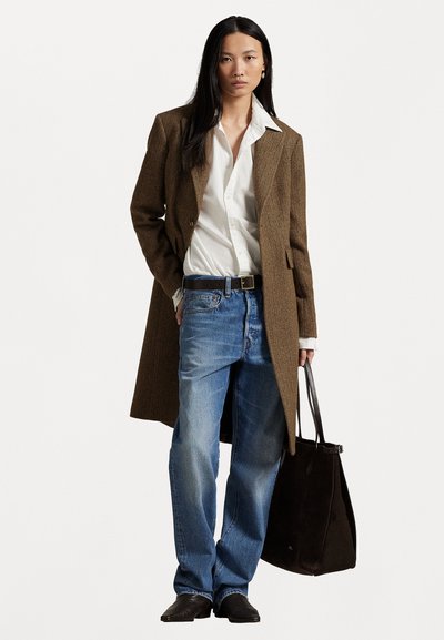 Brauner Fischgrät-Mantel über einem weißen Hemd, blauen Jeans und schwarzen Schuhen. Trägt eine schwarze Wildleder-Handtasche. Lange gerade schwarze Haare.