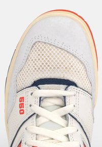 Baskets blanches avec dessus en daim gris et mesh, accents rouges, et semelle en caoutchouc beige. Dispose de lacets et du logo "550" sur le côté.