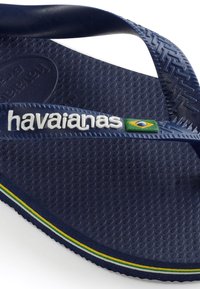 Sötétkék gumipapucs, textúrált talppal. A "havaianas" fehér logóval és zöld-sárga csíkkal a szélén rendelkezik.