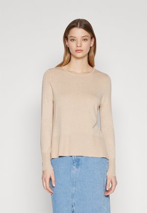 Maglione beige a maglia con maniche lunghe, scollatura rotonda e dettagli a coste. Vestibilità casual con una forma leggermente svasata. Abbinato a una gonna di jeans.
