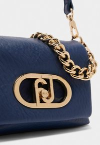 Borsa in pelle texturizzata blu navy con tracolla in catena dorata e un lucchetto ovale dorato con il nome del marchio. I dettagli includono un design del logo ben pronunciato.