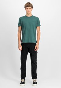 Tmavě zelené bavlněné tričko s kulatým výstřihem a krátkými rukávy, doplněné o černé cargo kalhoty s boční kapsou a černé tenisky.