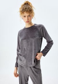 Grå velourpajamaställ med lång ärm, med vita prickiga detaljer. Mjuk textur och avslappnad passform, med raglanärmar och elastisk midja.