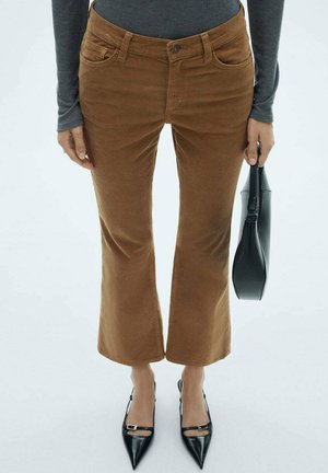 Bruine corduroy flare pants met vijf zakken en een knoopsluiting, gecombineerd met puntige zwarte hakken en een gestructureerde zwarte handtas.
