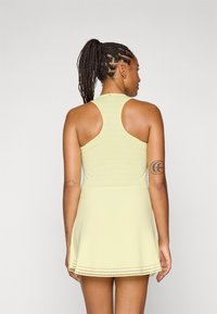 Vestido atlético amarelo-claro com corpete justo e saia fluida. Apresenta um design de costas nadadora e detalhes perfurados na barra.