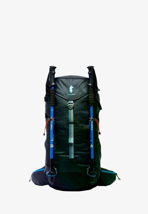 Black Cotopaxi hiking backpack with attached blue trekking poles secured by front straps, isolated on white background.