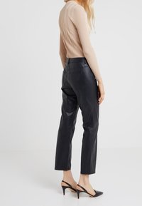 Haut beige à manches longues côtelé associé à un pantalon en cuir noir taille haute et des escarpins à talon ouvert noirs avec un accent rouge sur le talon.