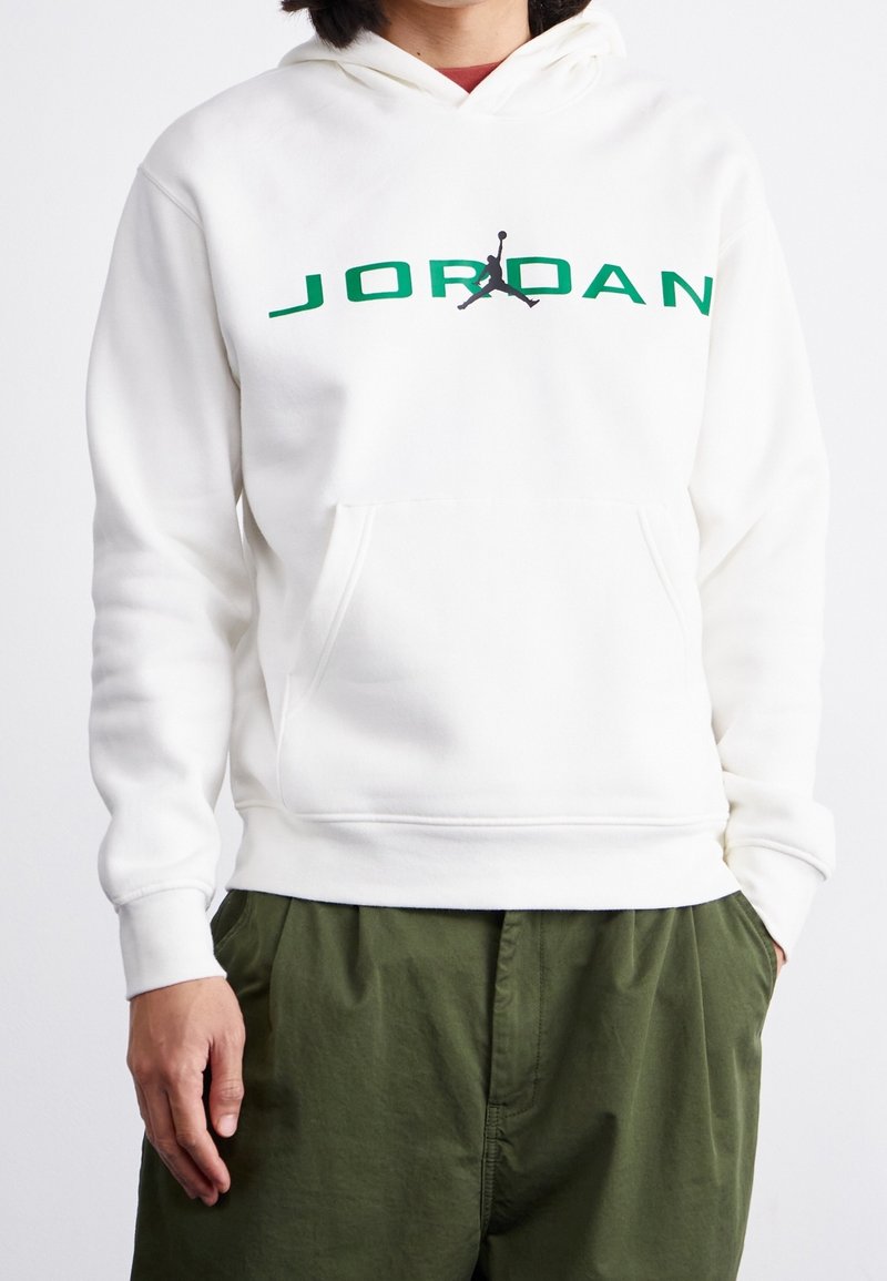 Felpa bianca con cappuccio caratterizzata da un logo "JORDAN" verde e un grafiche Jumpman nera, dotata di tasca frontale e polsini a costine. Abbinata a pantaloni verdi.