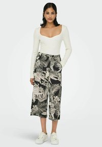 White long-sleeve bodysuit with a deep scoop neckline paired with black culotte pants featuring a floral and leaf pattern in beige. White sneakers.