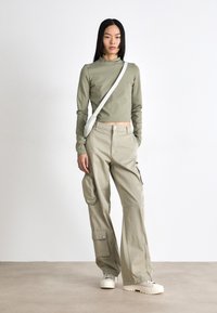 Olive green long-sleeve top and beige wide-leg cargo pants with multiple pockets. The model carries a white crossbody bag.