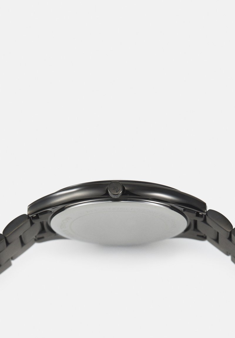 Vista lateral de un elegante reloj de pulsera de metal negro que muestra la corona del reloj y parte de la pulsera enlazada sobre un fondo blanco.