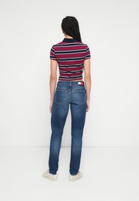 Prugasta bordo polo majica s kratkim rukavima, uparena s izblijedjelim plavim trapericama. Vidljiva etiketa na trapericama, jednostavne tenisice, neutralna pozadina.