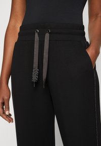 Melni sporta bikses ar auklu jostasvietā un metāla acīm. Aprīkotas ar logotipa detaļu uz auklām un sānu šuvju akcentiem.