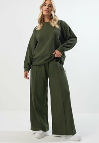 Olivgrön sweatshirt och vida byxor gjorda av mjukt tyg. Outfiten har en avslappnad passform och har långa ärmar samt en rund hals.