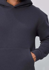 Sweat à capuche gris foncé en tissu doux, doté d'une grande poche kangourou et d'une capuche avec cordon de serrage pour un ajustement personnalisé. Texture lisse.