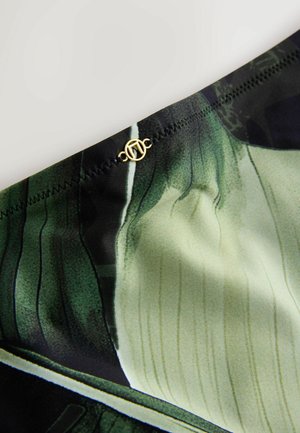 Zaļš un melns rakstains audums ar gludu tekstūru; jostasvietā ir zelta akcenta detaļa; dizainā iestrādātas plānas vertikālas līnijas.