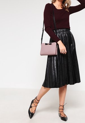 Jupe plissée en faux cuir noir, associée à un haut à manches longues bordeaux et des ballerines noires à lacets. Accessoires : un sac bandoulière rose.