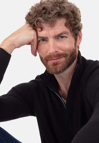 Schwarzer Reißverschluss-Pullover mit strukturierter Oberfläche, ausgestattet mit Kapuze und dezenten gerippten Akzenten. Das Model hat kurze lockige Haare und einen Bart.