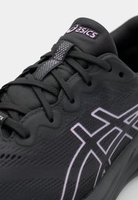Baskets de sport noires avec surface texturée et accents réfléchissants. Présente un laçage, un col rembourré et un logo proéminent en violet.