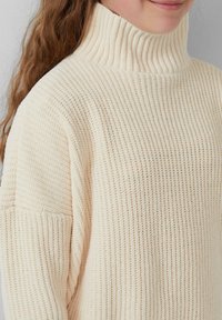Crème-kleurige gebreide trui met een hoge geribbelde kraag, een losse pasvorm en een gestructureerde stof met een subtiel patroon.