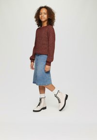 Bordeauxfarbener Strickpullover, hellblaue Jeansrock in knielanger Länge und weiße Kampfstiefel mit schwarzen Schnürsenkeln und Sohlen. Weiße Socken sind oberhalb der Stiefel sichtbar.